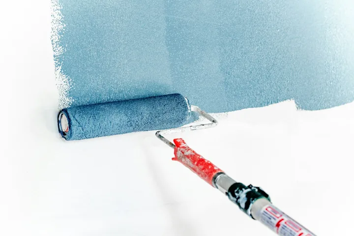 Paint roller applying blue paint to a white wall